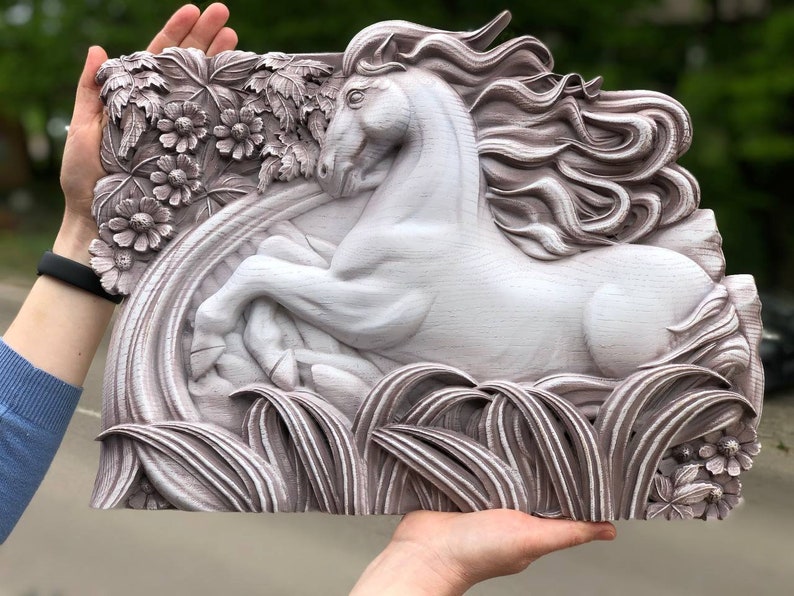 May include: A white wooden wall sculpture of a horse with flowing mane and tail, carved in a detailed style. The horse is surrounded by carved leaves and flowers, creating a whimsical and elegant design.