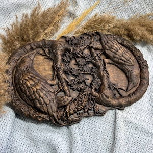 May include: A wooden wall hanging with a carved design of two birds intertwined around a tree with flowers. The birds are brown and the tree is dark brown.