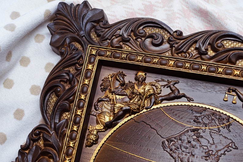 Puede incluir: Un marco de madera marr&oacute;n oscuro con detalles dorados y tallas intrincadas. El marco rodea una escultura en relieve de una figura a caballo, un ciervo y una balanza de la justicia. La escultura se coloca sobre un fondo de mapa del mundo.