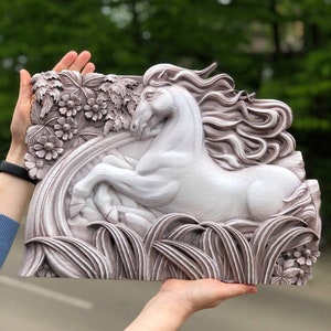 May include: A white wooden wall sculpture of a horse running through a field of flowers and grass. The horse has a flowing mane and tail. The sculpture is painted in a light brown colour.