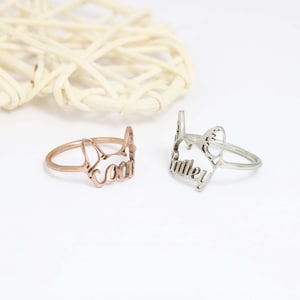 K&ouml;nnte beinhalten: Zwei Metallringe mit einem ausgeschnittenen Design in Form einer Katzenkopf-Silhouette. Ein Ring ist ros&eacute;goldfarben mit dem integrierten Namen Coco, der andere ist silberfarben mit dem integrierten Namen Bailey im Design.