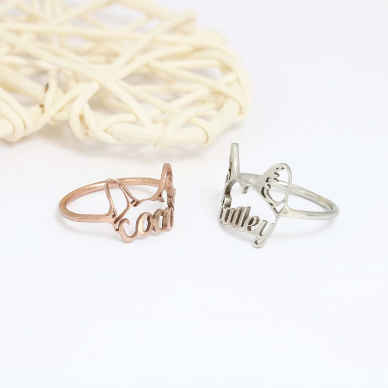 K&ouml;nnte beinhalten: Zwei Metallringe mit einem ausgeschnittenen Design in Form einer Katzenkopf-Silhouette. Ein Ring ist ros&eacute;goldfarben mit dem integrierten Namen Coco, der andere ist silberfarben mit dem integrierten Namen Bailey im Design.
