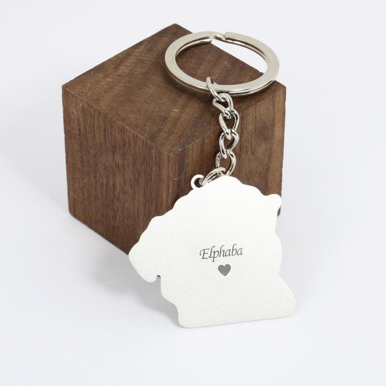 May include: Silver keychain with a lion silhouette and the name "Elphaba" engraved on it. The keychain is attached to a silver ring and chain.
