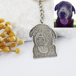 May include: Silver keychain with a black and white engraved image of a dog's head. The dog is sticking its tongue out and has a happy expression.