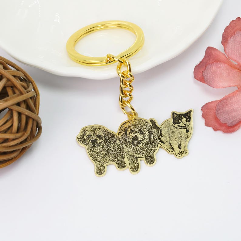 May include: Gold keychain with a photo engraved of two dogs and a cat. The keychain has a gold ring and chain.