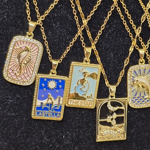 May include: Five gold necklaces with different pendants featuring colorful enamel and rhinestones. The pendants are rectangular and feature images of a seahorse, a woman with a star, a woman with a moon, a woman with a sun, and a dolphin. The pendants have the words "LASTELLA", "THE STAR", and "KNIGHT OF SWORDS" written on them.