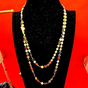 Könnte beinhalten: Eine goldene Halskette mit zwei Strängen runder, münzförmiger Glieder. Die Halskette wird auf einer schwarzen Samt-Mannequin-Büste präsentiert.