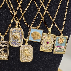 May include: A set of gold necklaces with various pendants featuring colorful enamel and rhinestones. The pendants include a dolphin, a seashell, a tarot card with the Wheel of Fortune, and a tarot card with the Sun.