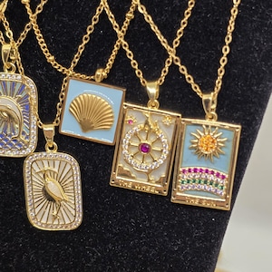May include: Four gold necklaces with different pendants. The pendants are square and feature a seashell, a sun, a wheel, and a bird. Each pendant is decorated with rhinestones and colorful gems.