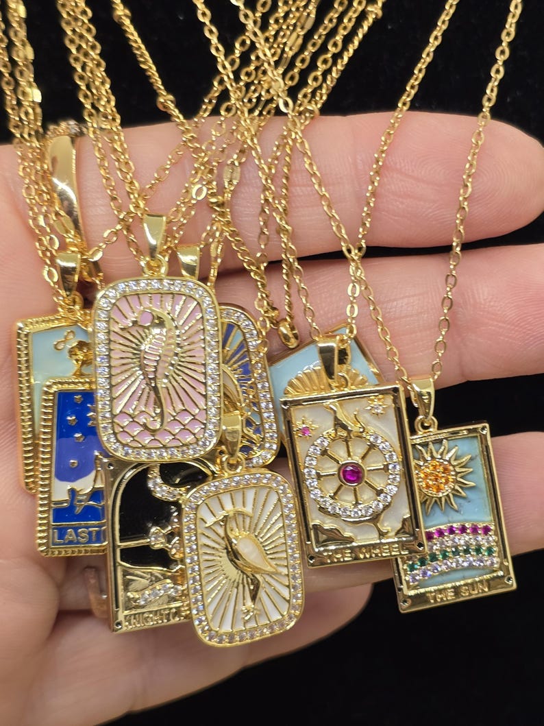 May include: A set of gold necklaces with colorful enamel pendants featuring tarot card imagery. The pendants are rectangular and have a gold frame with clear rhinestones. The pendants feature images of the Sun, the Wheel, the Knight of Swords, the Last Judgement, and the High Priestess.