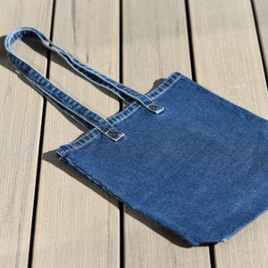 Peut inclure: Un sac fourre-tout en denim bleu avec des anses assorties. Le sac est rectangulaire avec un design simple et des coutures visibles. Les anses sont fixées avec des coutures renforcées.