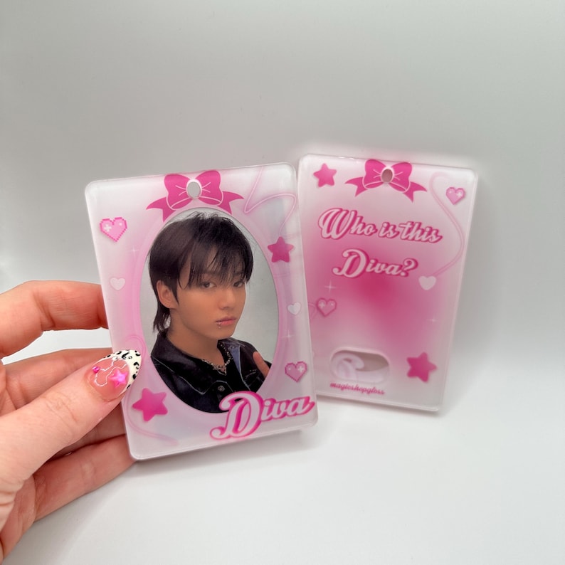 May include: A pink and white plastic card with a photo of a person in a black jacket and a pink bow on top. The text "Who is this Diva?" is on the right side of the card. The text "Diva" is on the left side of the card.