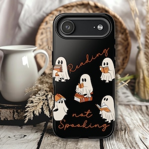 Può includere: Custodia per telefono nera con fantasmi dei cartoni animati che leggono libri. Le parole "Reading not Spooking" sono scritte in arancione. La custodia ha un obiettivo e un flash.