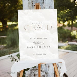 May include: A baby shower welcome sign on an easel. The sign features the text "We are on Cloud Nine" and "Welcome to Madison's Baby Shower" with the date September 25, 2026. The background has a cloud design.