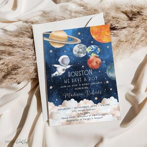 May include: A blue and gold baby shower invitation with a cartoon astronaut holding balloons shaped like planets. The text reads "Houston, We Have A Boy" and includes the baby's name, Madison Roberts, and the date and time of the shower.