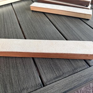 May include: A rectangular sharpening stone with a light tan, textured surface and a wooden base. Several similar stones are visible, suggesting a set or collection of woodworking tools.