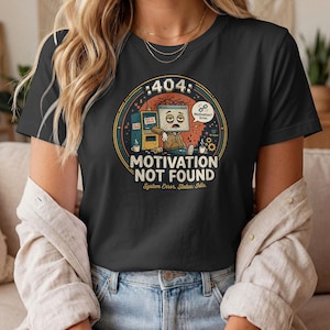 Könnte beinhalten: Ein schwarzes T-Shirt mit einem Grafikdruck eines müden Computermonitor-Charakters, der neben einem defekten Automaten sitzt. Der Text lautet 404, MOTIVATION NOT FOUND und System Error. Status: Idle. Eine Sprechblase sagt Motivation? Error.