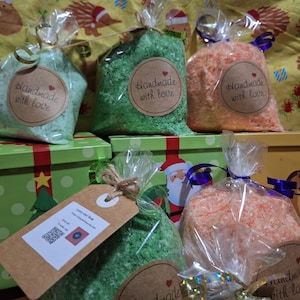 May include: Bags of colorful bath salts in green, orange, and light green, each sealed in clear cellophane and tied with a ribbon. Each bag has a brown tag that says "Handmade with love". The bags are on top of green and yellow gift boxes.