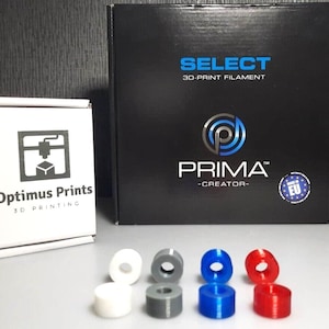 Op de afbeelding: Een close-up van tien spoelen 3D-printerfilament in verschillende kleuren, waaronder wit, grijs, blauw en rood. De spoelen zijn gerangschikt in twee rijen van vijf. De spoelen zijn gelabeld met "SELECT 3D-PRINT FILAMENT" en "PRIMA CREATOR".