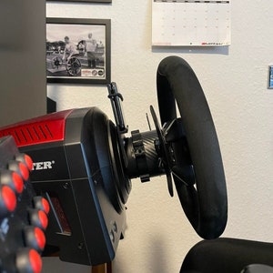 Può includere: Un volante da corsa nero con una base rosso e nera e un pannello di pulsanti rosso e nero. Il volante è montato su un supporto ed è collegato a un computer.