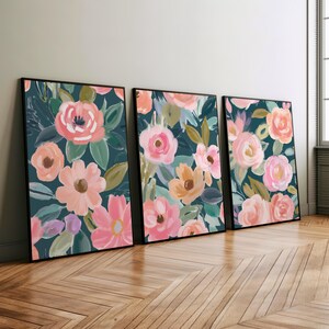 Op de afbeelding: Drie ingelijste prints met een bloemenmotief. De prints hebben een donkerblauwe achtergrond met roze, perzikkleurige en oranje bloemen. De lijsten zijn zwart.