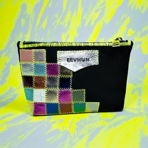 Può includere: Pochette nera con cerniera e design patchwork sul davanti. Il patchwork presenta quadrati di vari colori, tra cui rosa, blu e argento, cuciti insieme con filo giallo. La pochette ha un'etichetta argentata con la scritta "EEVHUN".