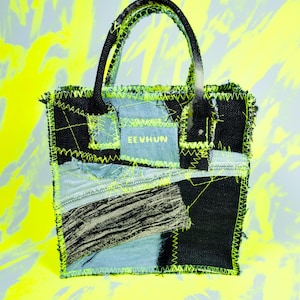 Può includere: Una borsa tote patchwork con un design in denim nero e azzurro. La borsa presenta cuciture verde neon e un manico nero. Il testo "EE VHUN" è visibile su una toppa azzurra.