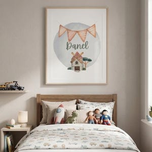 May include: A framed watercolor print with the name "Danel" above a whimsical illustration of a windmill and trees. The print hangs above a bed with a patterned comforter, pillows, and stuffed toys.