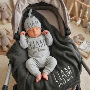 May include: A newborn baby wearing a gray hat and onesie, both embroidered with the name "LIAM" and the last name "jackson". The baby is lying in a stroller, covered with a gray blanket also embroidered with the name "LIAM jackson".