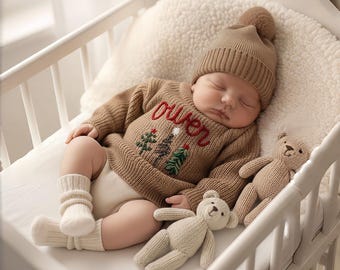 Pode incluir: Um bebé a dormir num berço, usando um camisola castanha com o nome "Owen" bordado a vermelho e motivos de árvores de Natal. O bebé também usa um chapéu castanho a condizer com um pompom e está perto de dois ursinhos de peluche.