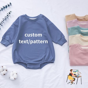 May include: A light blue long-sleeved baby onesie with the text "custom text/pattern" printed on the front. The onesie is shown on a white background with other onesies in different colours stacked in the background.