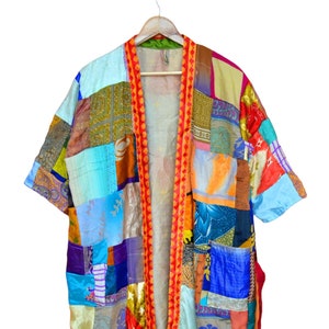 May include: A long, colorful patchwork kimono with a red and orange trim. The kimono is made of various fabrics and patterns, including floral, paisley, and geometric designs.