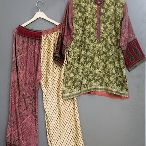 May include: A two-piece outfit consisting of a long-sleeved tunic and wide-leg trousers. The tunic features an olive green floral print with a dark red collar and sleeves. The trousers combine a cream-colored small floral print with dark red paisley panels.