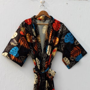 Pode incluir: Um quimono preto com estampa de folhas tropicais coloridas. O quimono tem um cinto de amarrar e mangas curtas.