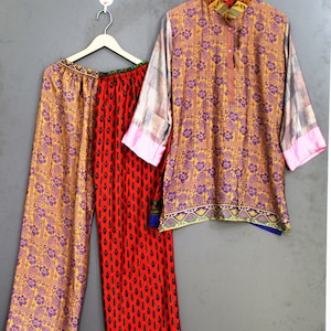 Könnte beinhalten: Ein zweiteiliges Outfit bestehend aus einem langärmeligen Hemd und einer Hose mit weitem Bein. Das Hemd zeigt ein gelb-violettes Blumenmuster mit karierten Ärmeln. Die Hose hat ein geteiltes Design mit einem gelben Blumenbein und einem roten Bein mit schwarzen Tropfenmotiven.