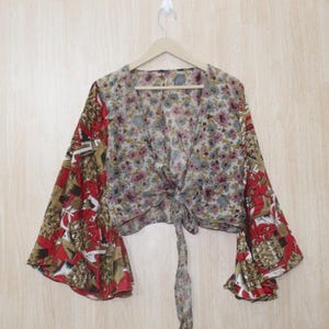 Könnte beinhalten: Eine Bluse mit Blumenmuster, einem Bindeband vorne und langen Glockenärmeln. Die Ärmel sind aus einem anderen Stoff mit einem geometrischen Muster in Rot, Gold und Weiß.