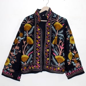 Pu&ograve; includere: Giacca nera con ricami floreali gialli, rosa e blu. La giacca presenta un collo alto e un'apertura frontale. Il design floreale &egrave; dettagliato e copre il davanti e le maniche. La giacca &egrave; appesa a una gruccia di legno.