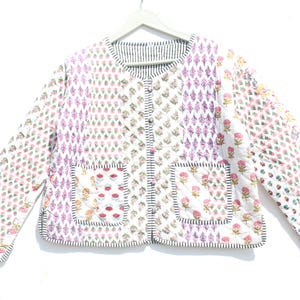 Könnte beinhalten: Eine weiße gesteppte Jacke mit Blumendruck und zwei aufgesetzten Taschen. Die Jacke hat einen Knopfverschluss und einen gestreiften Kragen.