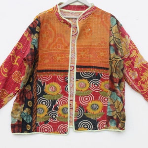 Könnte beinhalten: Eine bunte Patchworkjacke mit Stehkragen und langen Ärmeln. Die Jacke besteht aus verschiedenen Stoffen mit unterschiedlichen Mustern, darunter Blumen, geometrische Muster und Paisley. Die Jacke ist gesteppt und hat einen hellcremefarbenen Besatz.