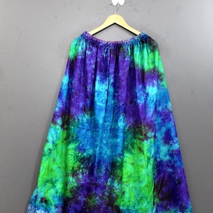 Könnte beinhalten: Ein langer, fließender Rock mit einem lebendigen Batikmuster in den Farben Dunkelviolett, leuchtendes Türkis und Limettengrün. Das Kleidungsstück hat einen elastischen Bund und eine weit ausgestellte Silhouette an einem Holzkleiderbügel.