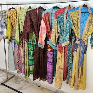 Könnte beinhalten: Eine Sammlung von acht bunten Seidenroben, die an einem Gestell hängen. Die Roben sind aus Patchwork-Stoff mit verschiedenen Mustern und Farben, darunter Grün, Blau, Rot, Gelb und Lila.