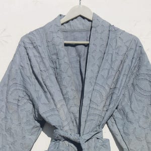 Könnte beinhalten: Eine hellblaue gesteppte Robe mit Blumenmuster. Die Robe hat einen Schalkragen und einen Bindegürtel.