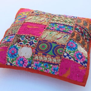 Puede incluir: Una almohada de patchwork colorida con un borde naranja brillante. La almohada est&aacute; hecha de varias telas y presenta bordados intrincados y lentejuelas.