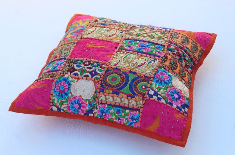 Puede incluir: Una almohada de patchwork colorida con un borde naranja brillante. La almohada est&aacute; hecha de varias telas y presenta bordados intrincados y lentejuelas.