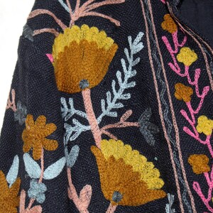 Pu&ograve; includere: Primo piano di un tessuto blu navy con motivi floreali ricamati. Il design presenta grandi fiori gialli e marroni, accenti rosa e gialli e foglie azzurre. Il ricamo &egrave; dettagliato e colorato.