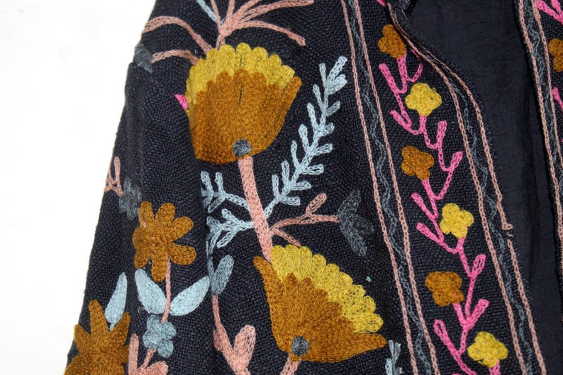 Pu&ograve; includere: Primo piano di un tessuto blu navy con motivi floreali ricamati. Il design presenta grandi fiori gialli e marroni, accenti rosa e gialli e foglie azzurre. Il ricamo &egrave; dettagliato e colorato.