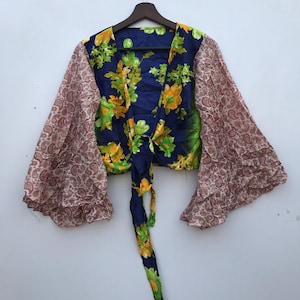 Op de afbeelding: Een blauwe en groene bloemenprint crop top met een strik aan de voorkant en wijde mouwen. De mouwen zijn gemaakt van een paisley print stof.