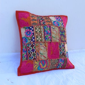 Puede incluir: Una funda de coj&iacute;n de patchwork colorido con un fondo rosa y bordados intrincados. La funda est&aacute; hecha de varias telas y presenta una variedad de colores, incluyendo rojo, naranja, amarillo, verde, azul y morado.