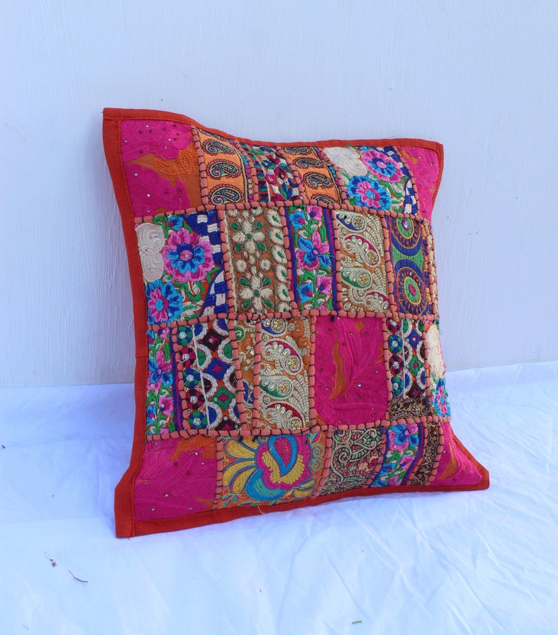 Puede incluir: Una funda de coj&iacute;n de patchwork colorido con un fondo rosa y bordados intrincados. La funda est&aacute; hecha de varias telas y presenta una variedad de colores, incluyendo rojo, naranja, amarillo, verde, azul y morado.