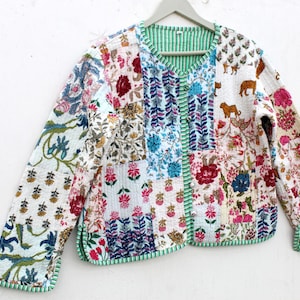 Könnte beinhalten: Patchwork-Jacke mit verschiedenen Blumen- und Tiermotiven in Rot-, Blau-, Rosa- und Grüntönen. Die Jacke hat ein grün gestreiftes Futter und einen Besatz. Sie hängt an einem Holzkleiderbügel.